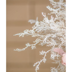Close-up of delicate white branching faux dried stems with a dusty pink ribbon tie visible at the base, against a warm terracotta background