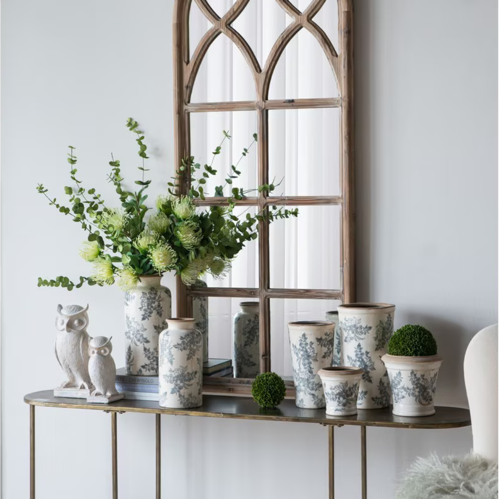 Jardin Toile ceramic vase collection displayed on a console table beneath an arched timber mirror with owl figurines and moss balls