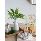 Aegean ceramic vase with fern fronds styled in a rattan tray on a timber coffee table alongside a gold coral branch ornament, wooden bead garland, hourglass, and coral fish figurine