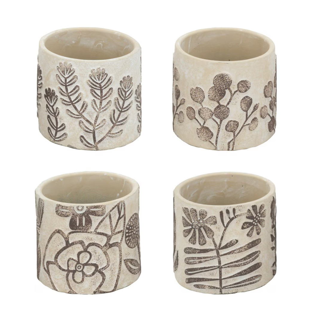 Set of four small cream ceramic pots each with a different hand-etched botanical design — fern sprig, eucalyptus branch, poppy with bee, and wildflower with fern — in stone-cream matte ceramic with brown etching, photographed on white background