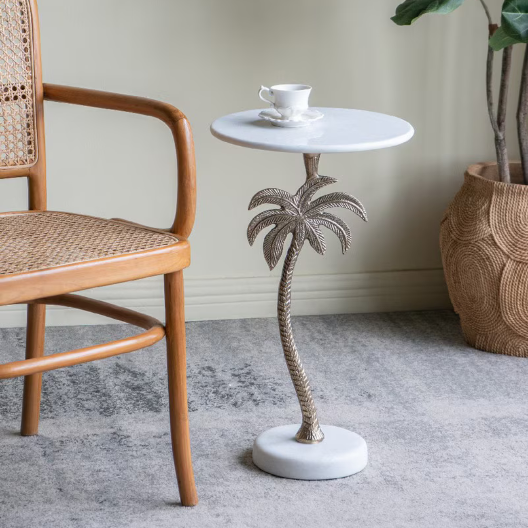 Small round side table with a marble top and palm tree design on the leg next to a wooden chair.
