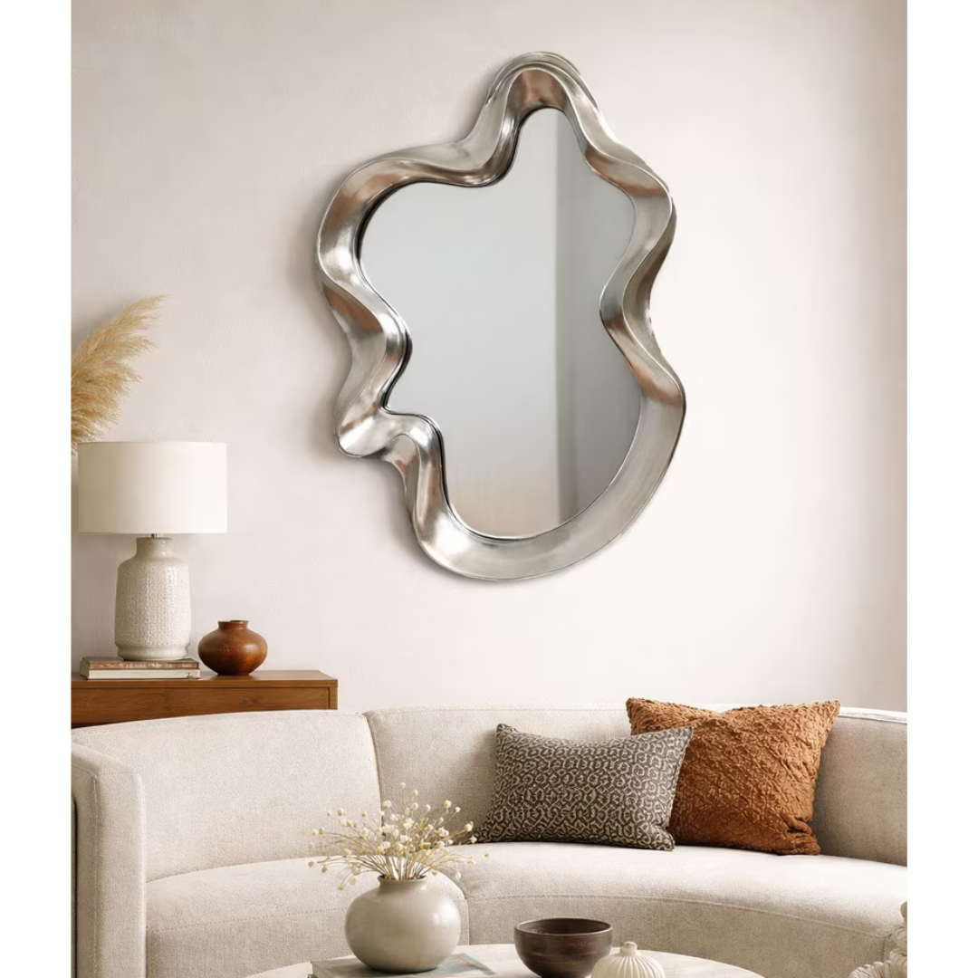 Silver sculptural wavy mirror hung above sofa in neutral living room styled with timber console and earthy cushions — Mish Lifestyle NZ