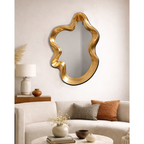 Gold sculptural wavy mirror hung above sofa in warm neutral living room styled with timber console and earthy cushions — Mish Lifestyle NZ