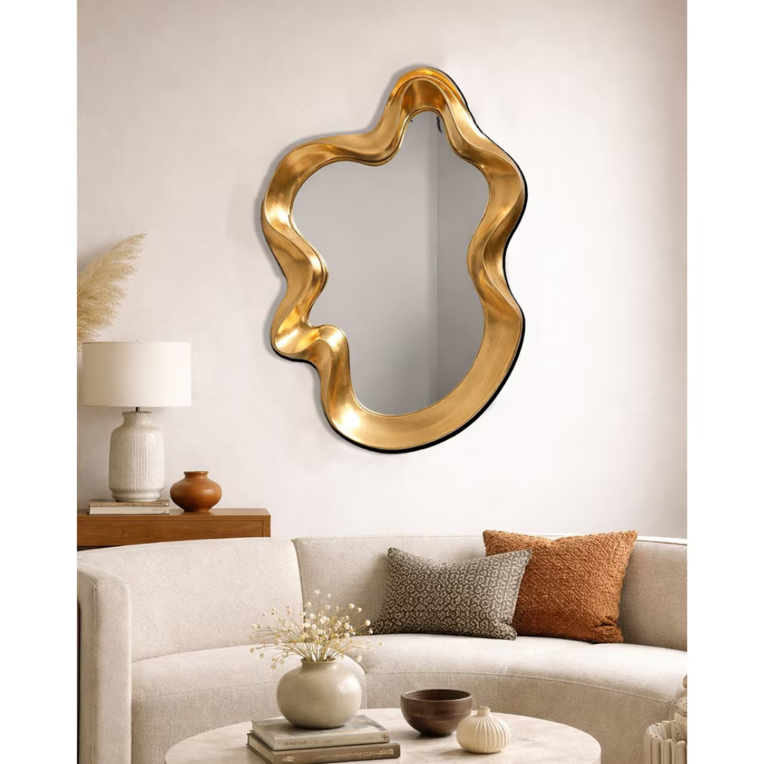 Gold sculptural wavy mirror hung above sofa in warm neutral living room styled with timber console and earthy cushions — Mish Lifestyle NZ